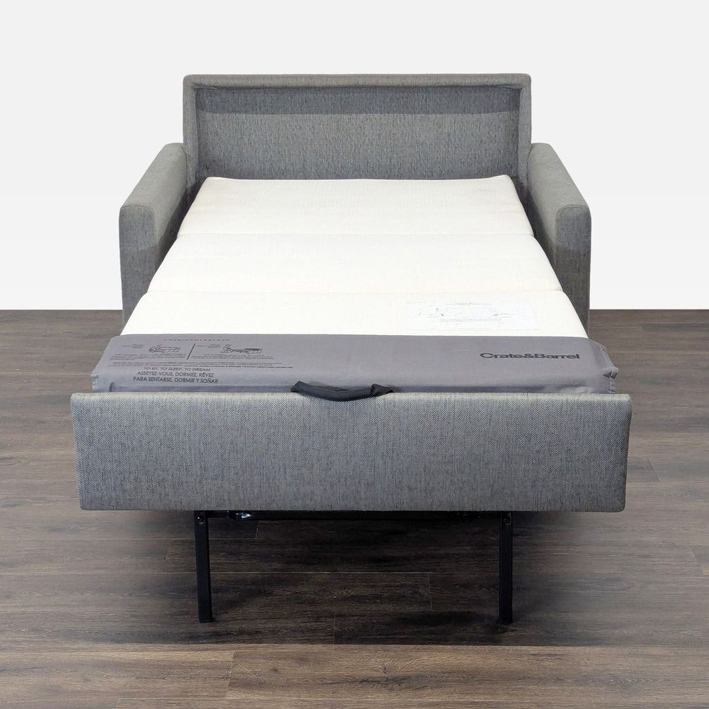 Gray Crate & Barrel sleeper sofa fully extended into a bed, shown against a wood floor and plain wall.  