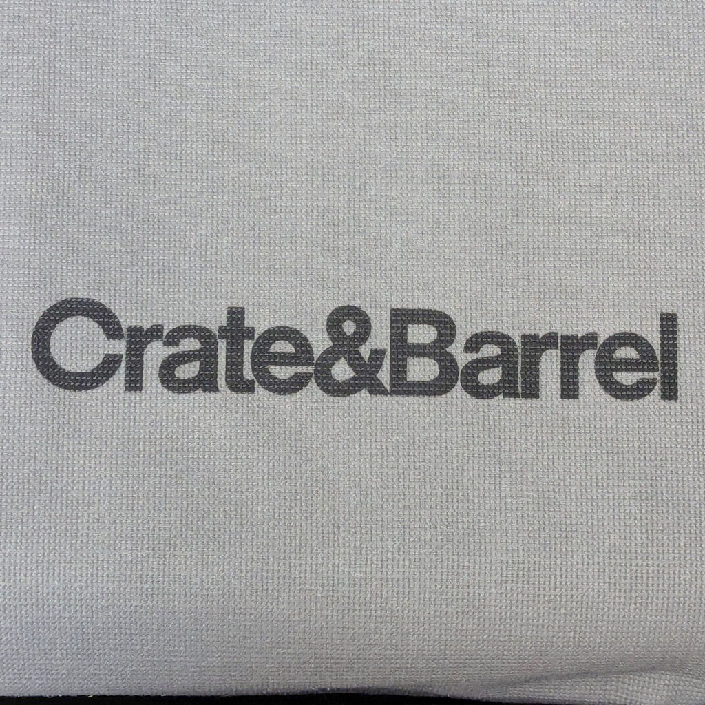 Close-up of Crate & Barrel logo printed on textured, light gray upholstery fabric from a sleeper sofa.  