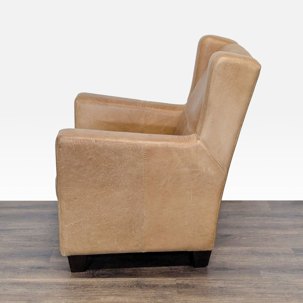 1. Side view of a tan leather West Elm lounge chair, showing its boxy shape and wooden legs on a wood floor.