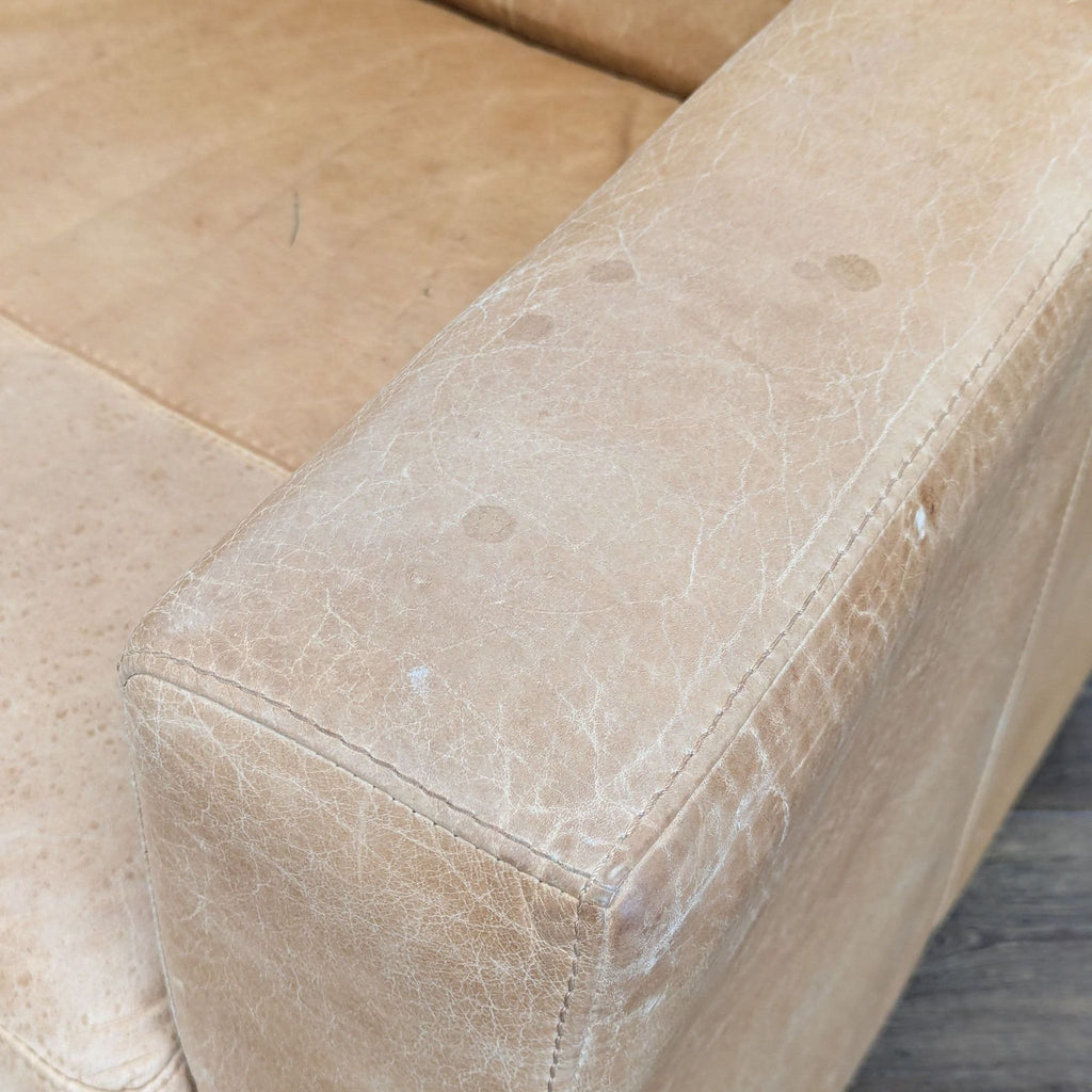 3. Detailed view of a West Elm lounge chair’s armrest, showing distressed tan leather with light stains and creases.