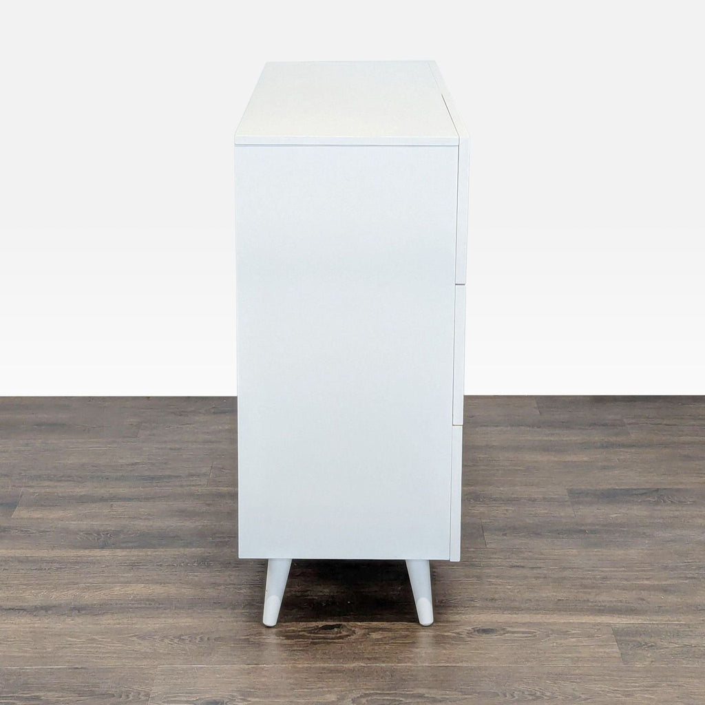 1. Side view of a white West Elm dresser with clean lines and angled legs, shown on a wooden floor.