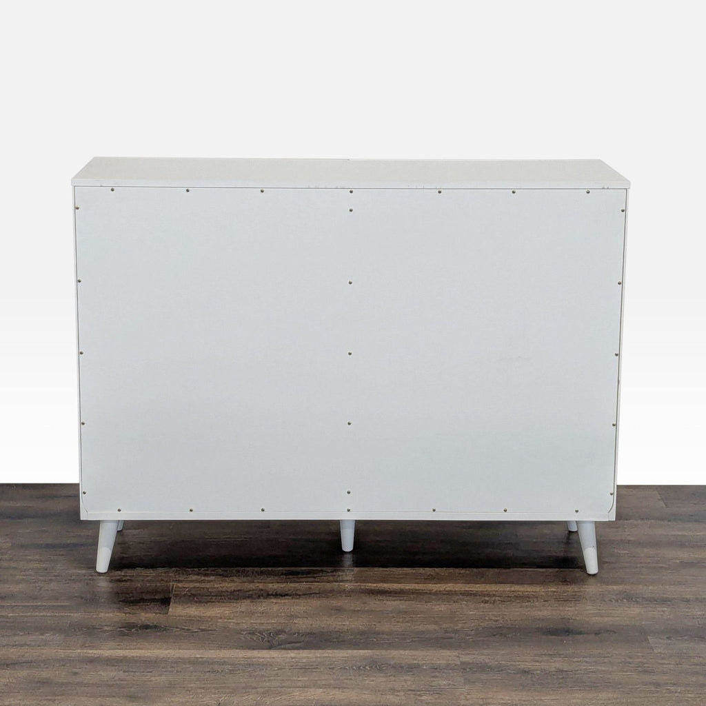 2. Back view of a white West Elm dresser with visible screws and four tapered legs, positioned on wood flooring.