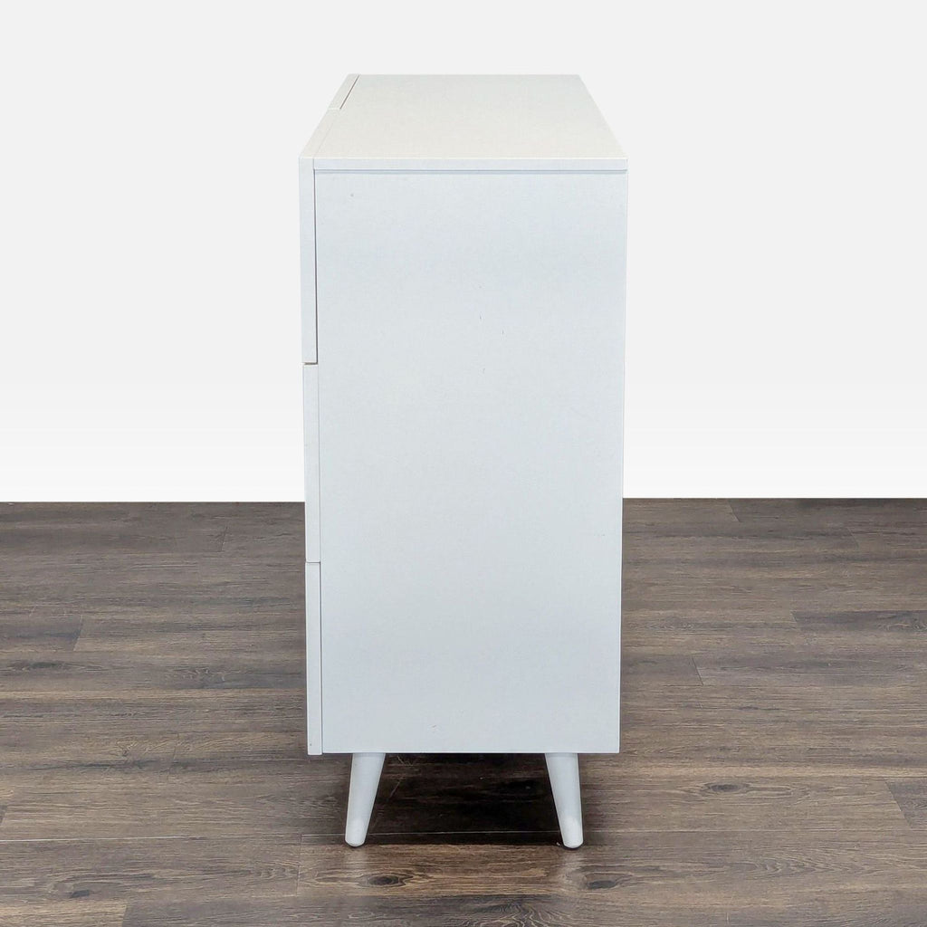 3. Opposite side view of a white West Elm dresser, showcasing its simple, modern profile and angled legs.