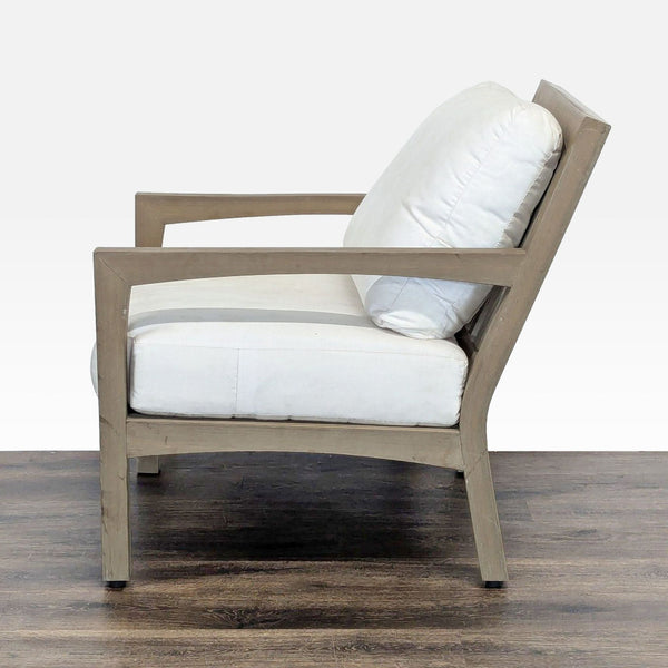 Side view of a Pottery Barn chair with a light wood frame and white cushions, placed on a wooden floor.  