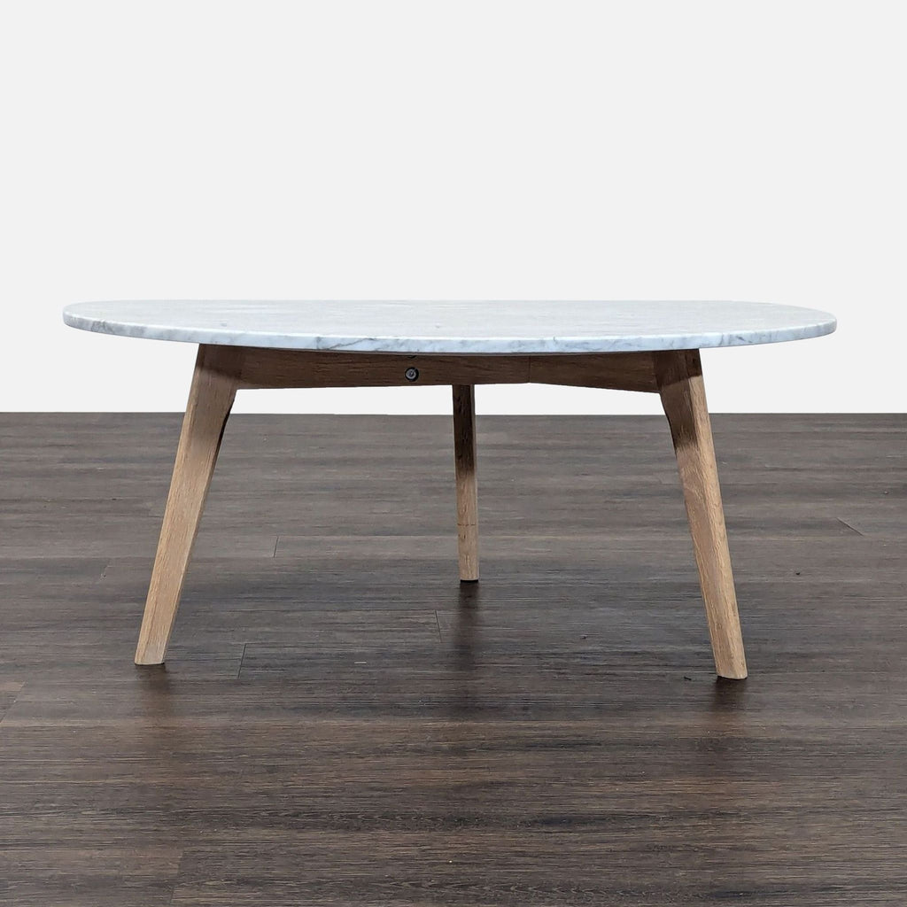 1. Side view of Article coffee table with a round marble top and angled oak legs on a wooden floor.  