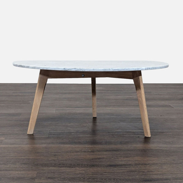 1. Side view of Article coffee table with a round marble top and angled oak legs on a wooden floor.  