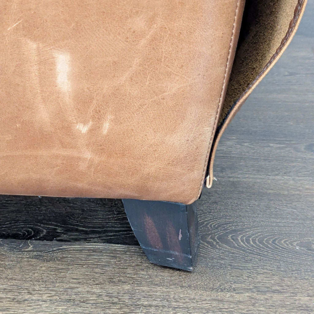 3. Close-up of the brown leather upholstery and dark wooden leg on a Pottery Barn lounge chair.