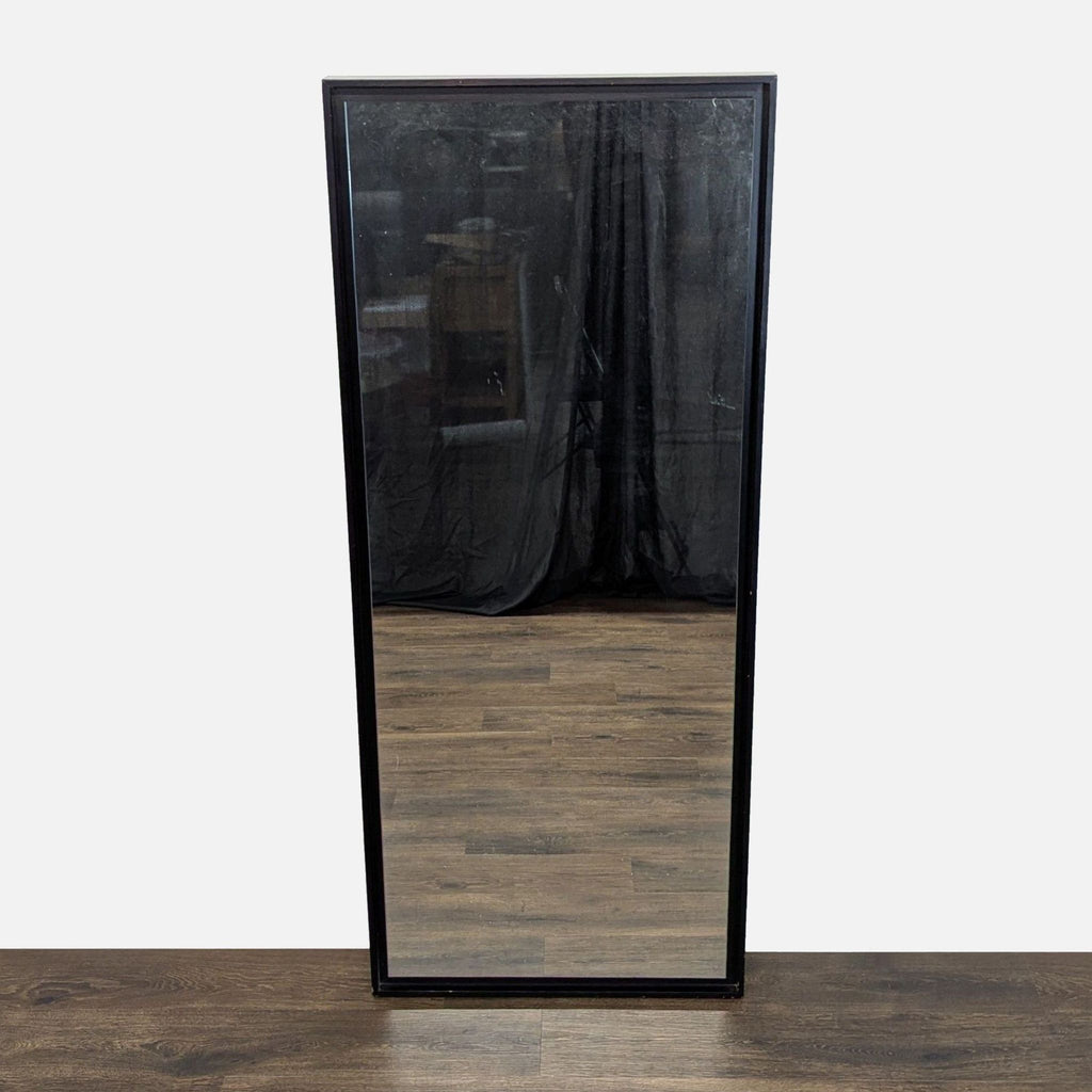 1. Rectangular West Elm mirror with a black frame, shown standing on a wooden floor with a dark background.