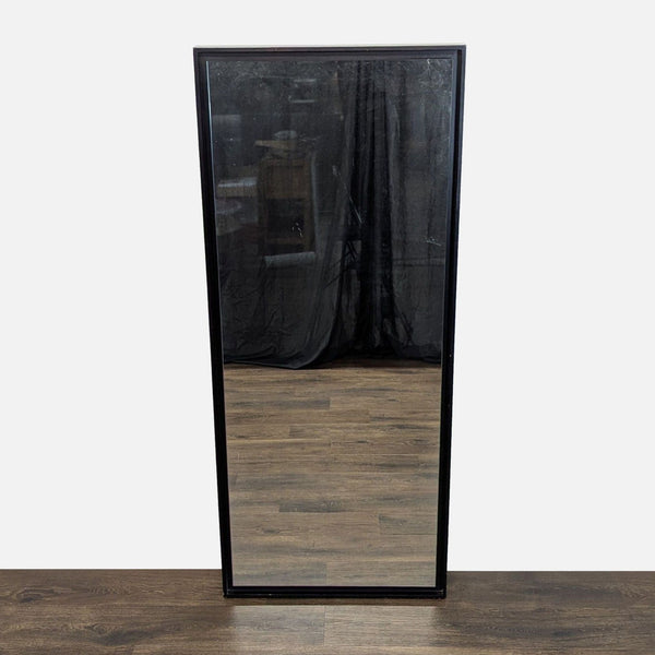 1. Rectangular West Elm mirror with a black frame, shown standing on a wooden floor with a dark background.