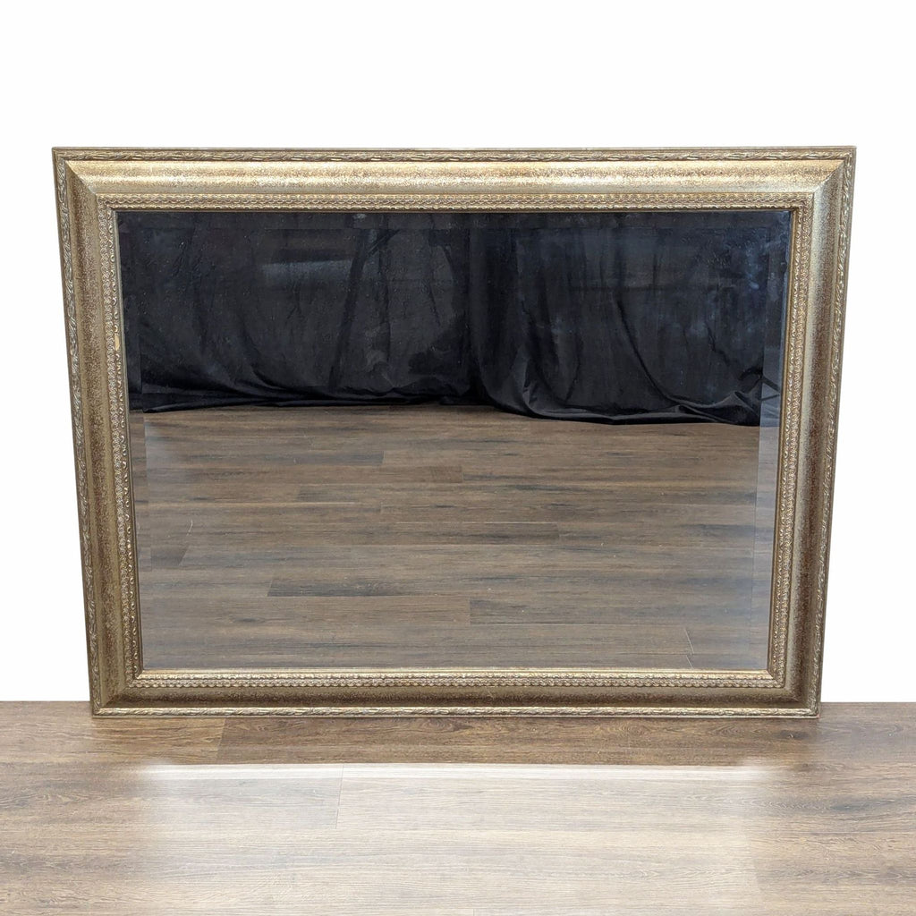 Rectangular Carolina Mirror with an ornate gold frame, displayed on a wooden floor with a dark backdrop.