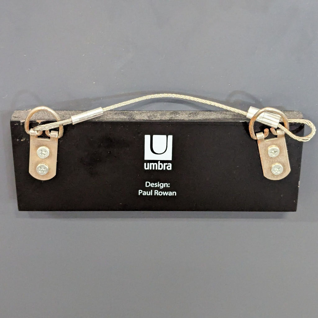 Back view of Umbra mirror featuring hanging hardware, a wire, and a designer label reading "Design: Paul Rowan."