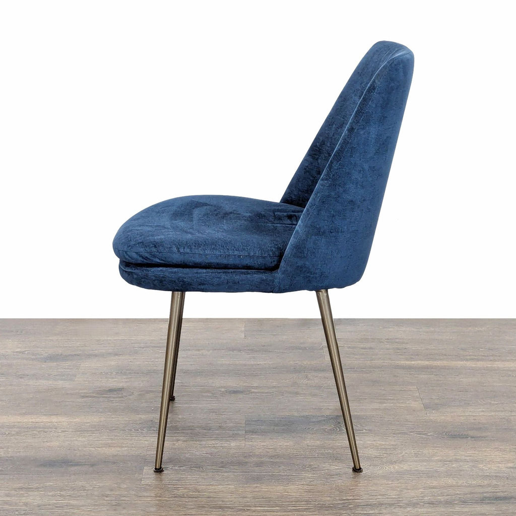 - Side profile of a West Elm dining chair with blue upholstery and slim metal legs on a wood floor.