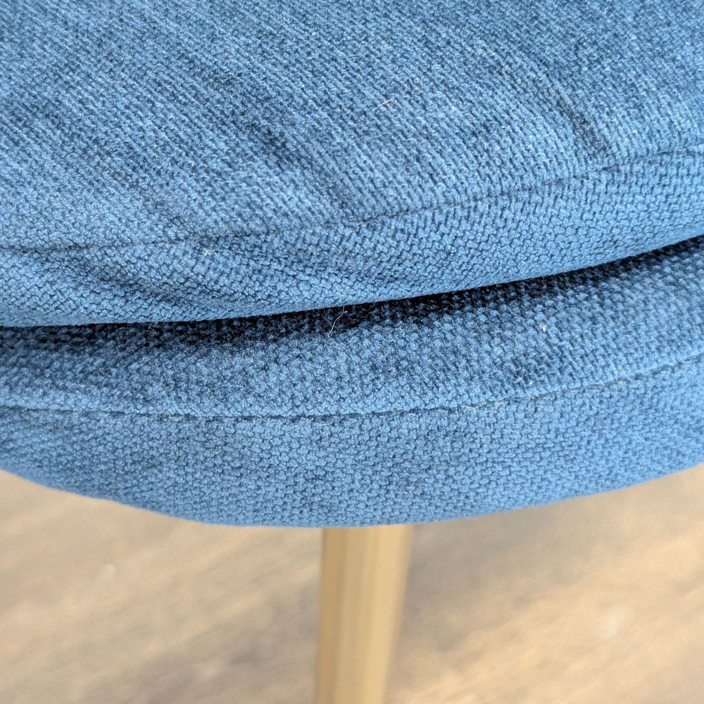 - Close-up of textured blue fabric upholstery and stitching on a West Elm dining chair seat cushion.