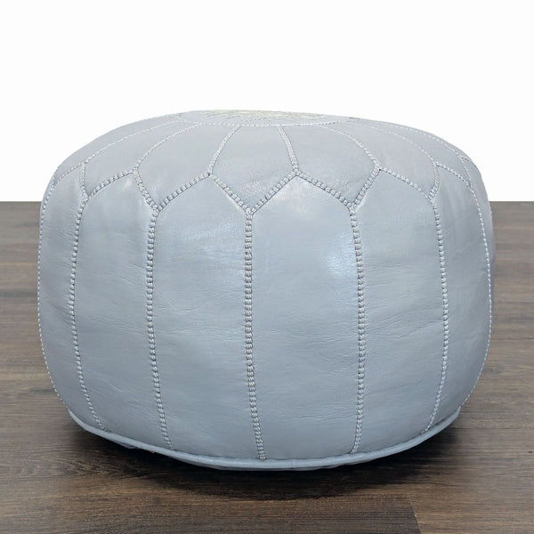1. Light grey leather ottoman from Reperch with distinct stitched panel design, shown on a wooden floor.