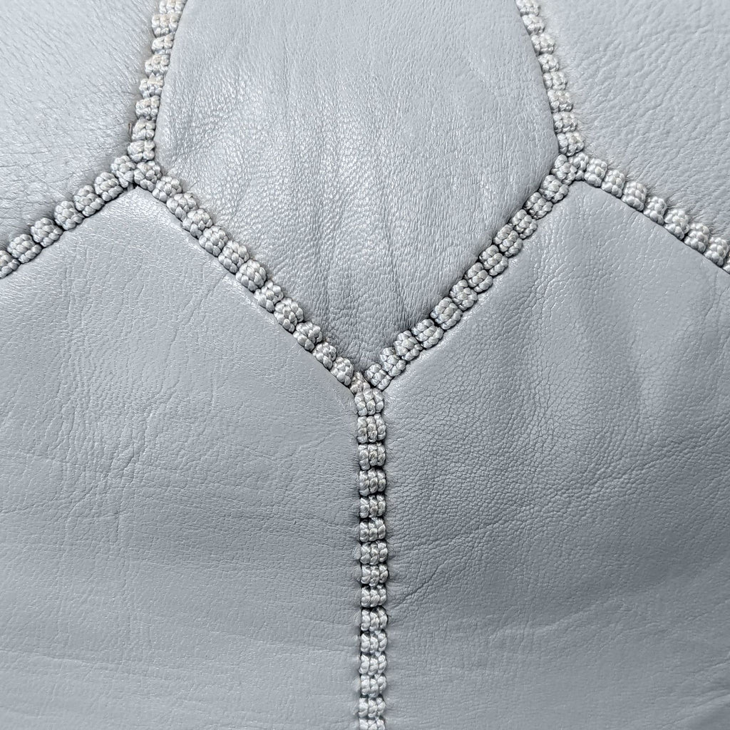 2. Close-up view of the detailed stitching on a light grey Reperch ottoman’s leather upholstery.