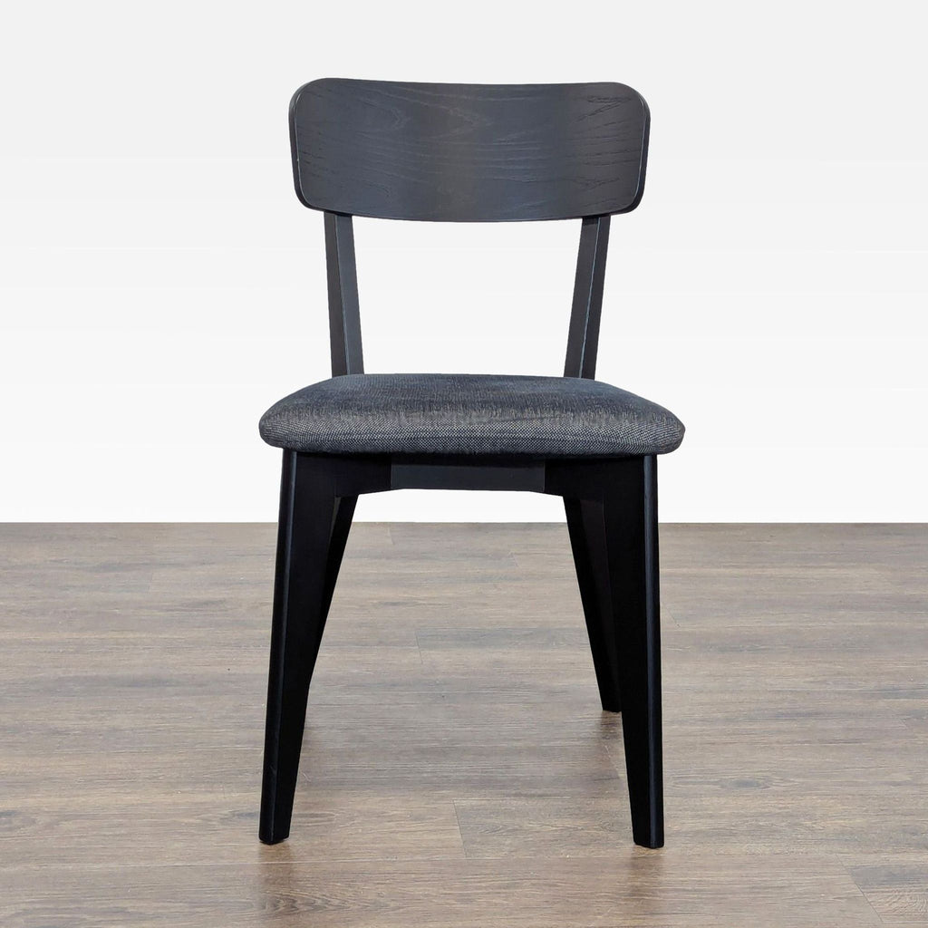 1. Front view of an Ikea dining chair with black wooden frame and cushioned dark seat on wood flooring.