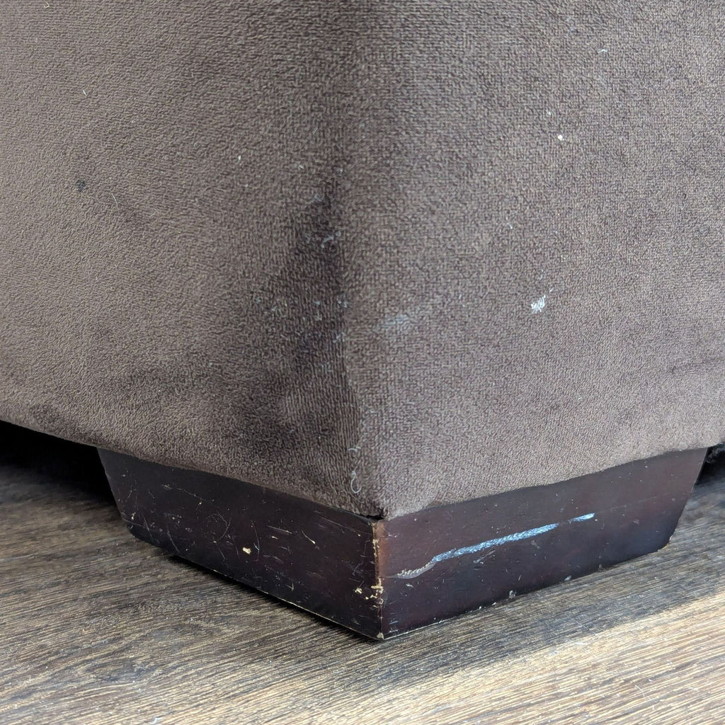 2. Bottom corner of Macy’s brown 3-seat sofa, with minor scuffs on wooden leg and some lint.
