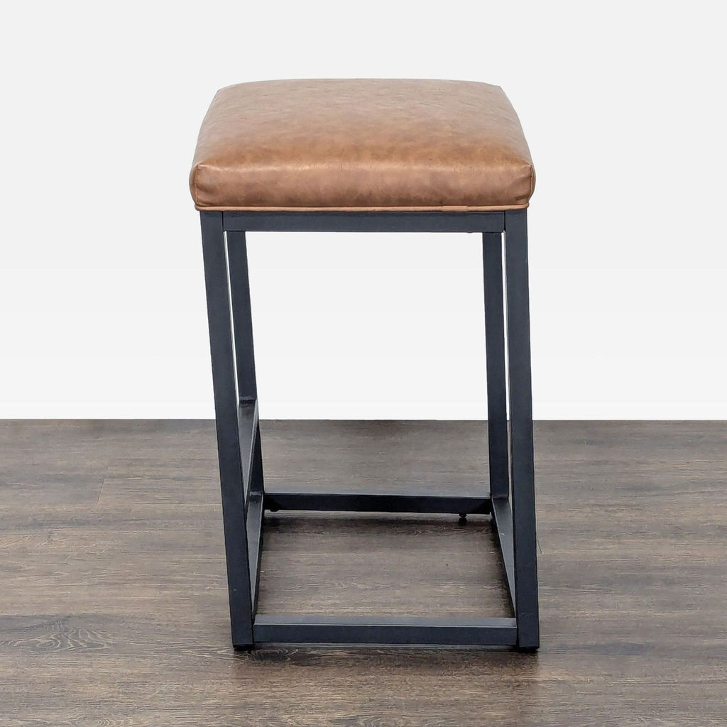 3. Square Bluefyn stool with black metal legs, footrest, and tan faux leather seat, angled perspective.