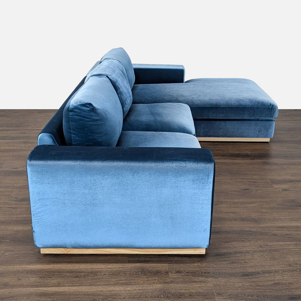 2. Side profile of a blue velvet Rove Concepts sectional, highlighting the plush armrests and wooden base.