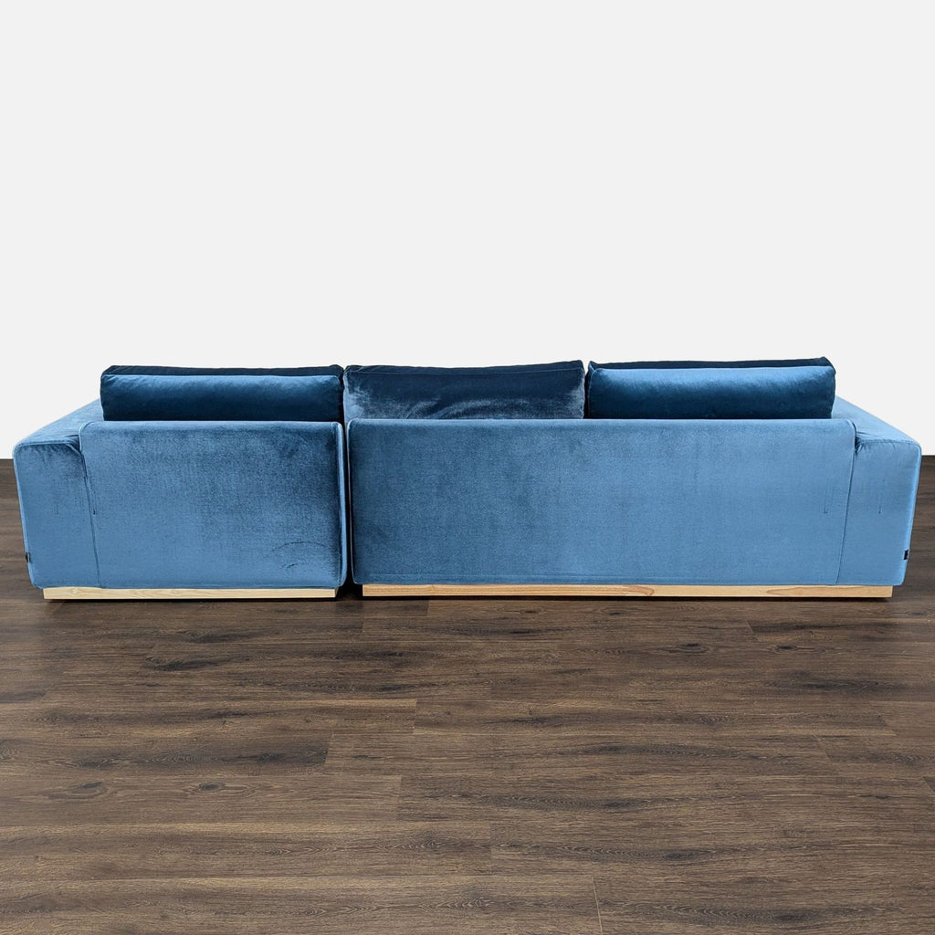 3. Back view of a blue velvet Rove Concepts sectional, emphasizing the sleek design and light wood trim.
