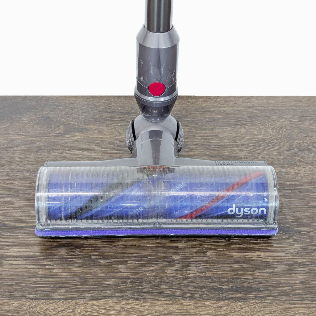 Close-up of Dyson vacuum roller head on hardwood floor, showing powerful brush for picking up dirt and debris.  