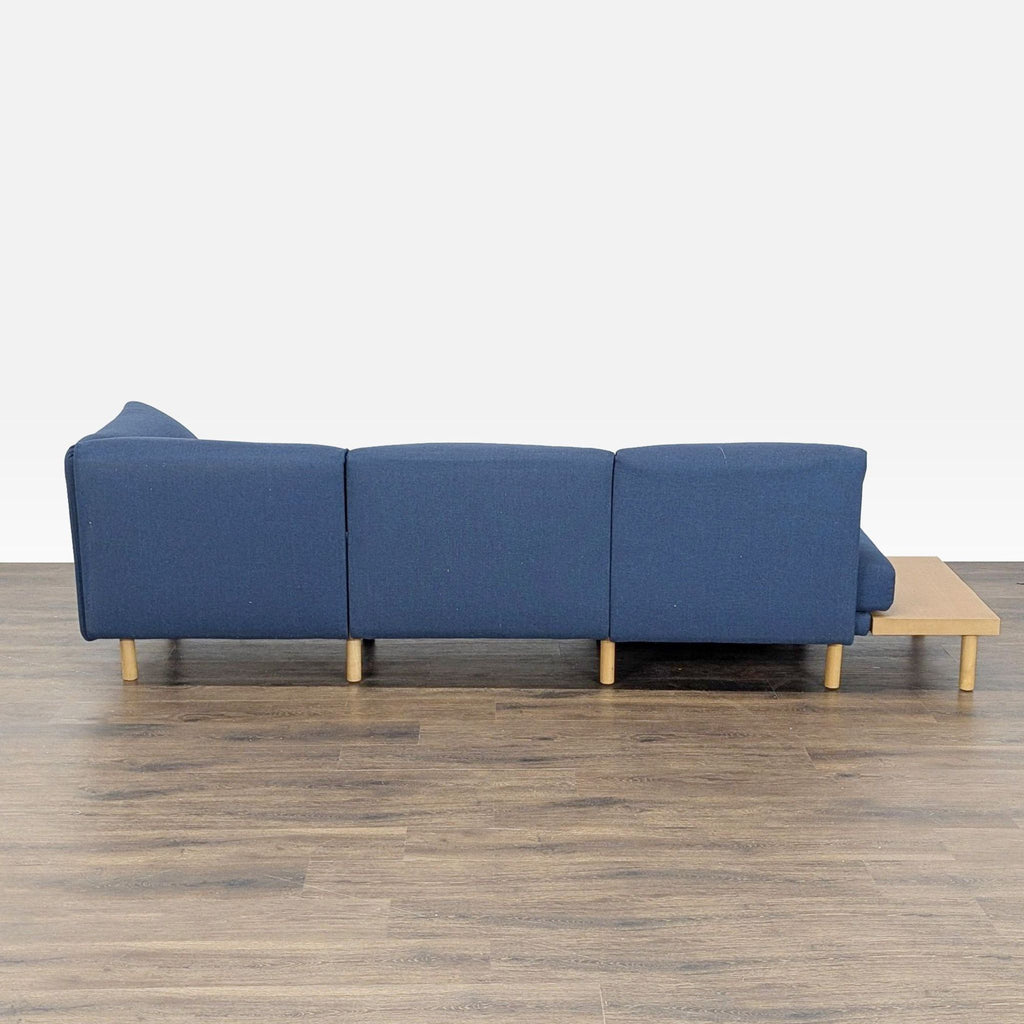 Rear view of the blue Burrow sectional sofa and side table, highlighting its clean lines and wooden legs.