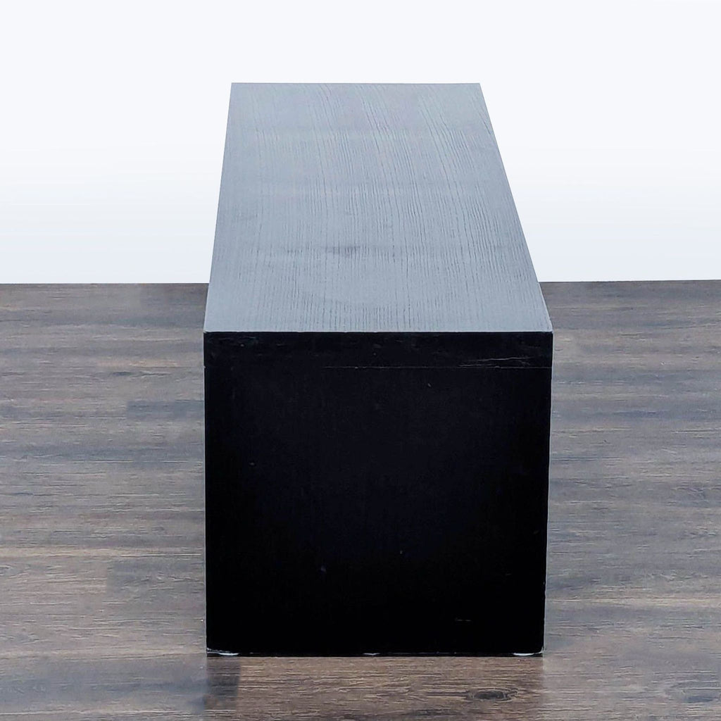 3. End view of a sleek black Reperch bench, with clean lines on a wood floor, minimalist look.