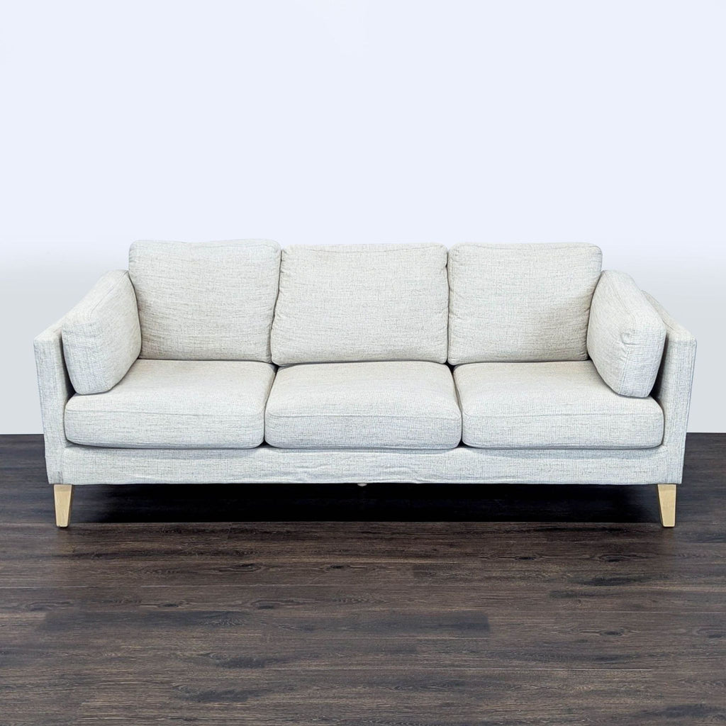1. Modern 3-seat World Market sofa with light gray upholstery and wooden legs, seen from the front on dark flooring.