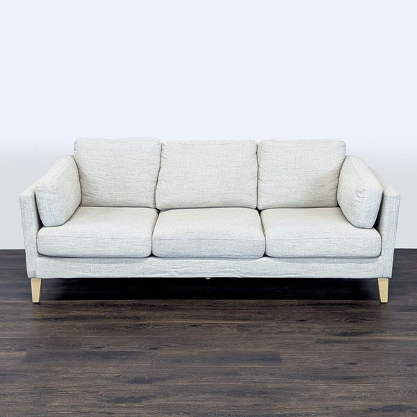 1. Front view of a Reperch 3-seat sofa with light upholstery and wooden legs on a dark wood floor.