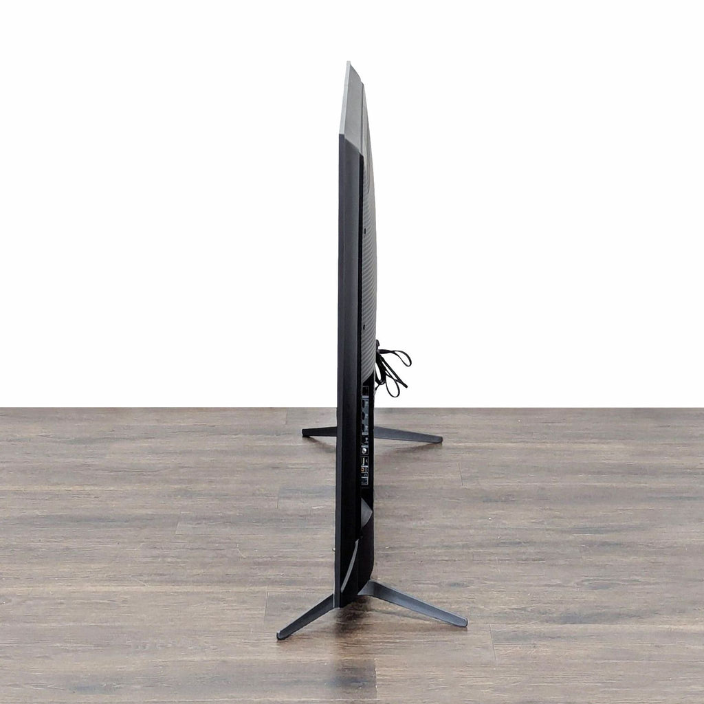 3. Side profile of a TCL 65" Smart TV highlighting its ultra-slim design and sturdy stand on a wooden floor.