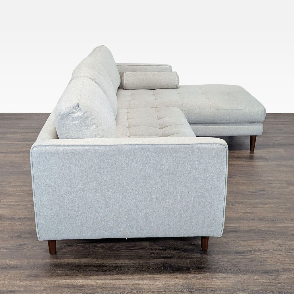 2. Side view of a modern Living Spaces sectional in light gray fabric, highlighting its clean lines and wooden legs.