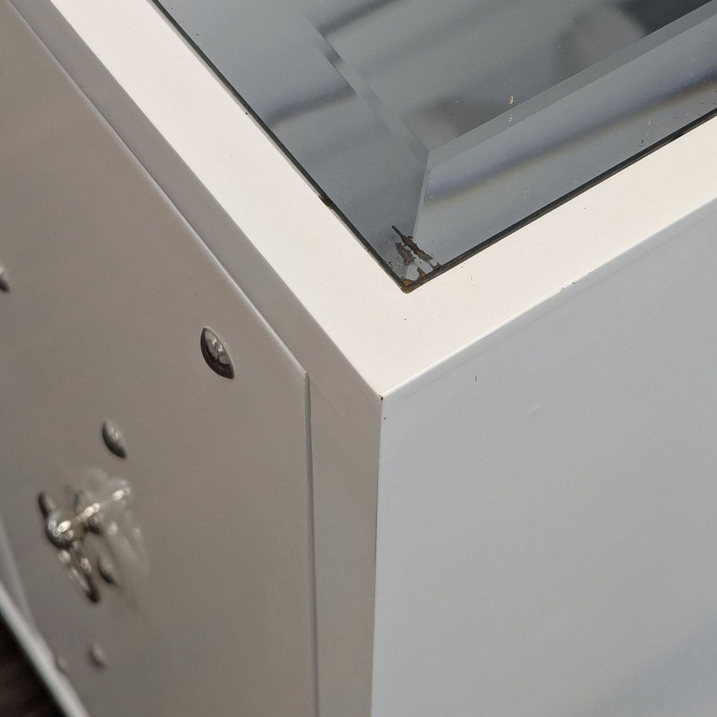 1. Close-up of the Reperch sideboard’s corner, showing a white surface with a glass top and minor wear.  