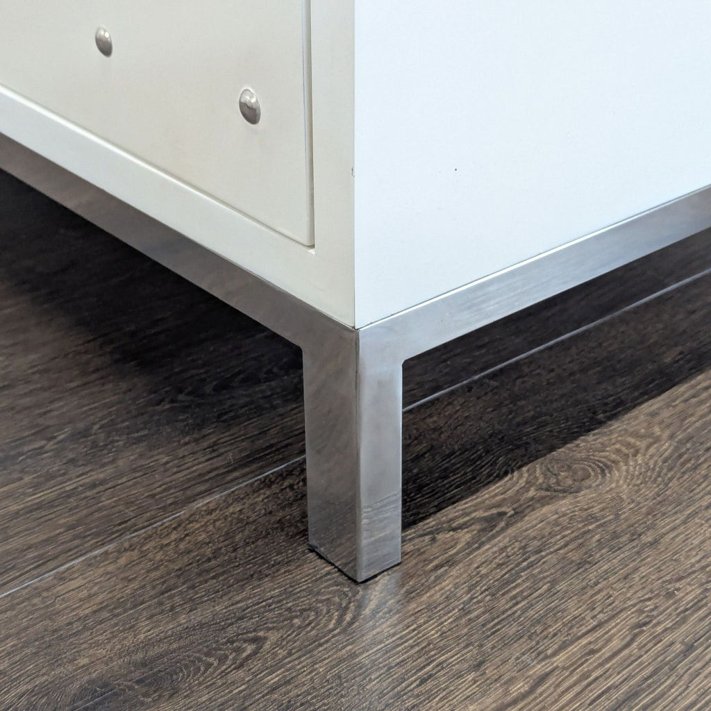 2. Metal leg detail of a Reperch credenza, featuring a white panel and silver hardware on a wood floor.  