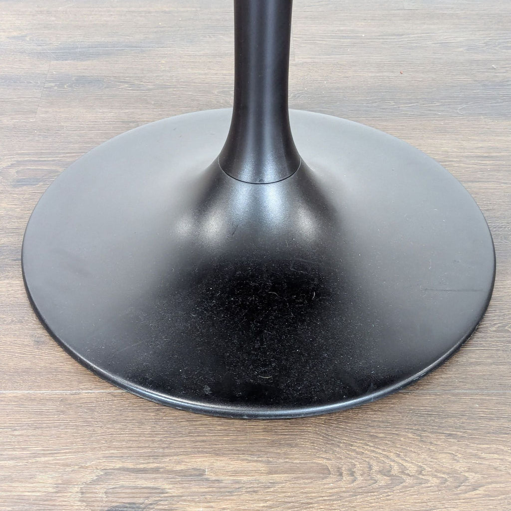 3. Close-up of the sturdy, round black powder-coated steel base of an Ikea dining table on wooden flooring.