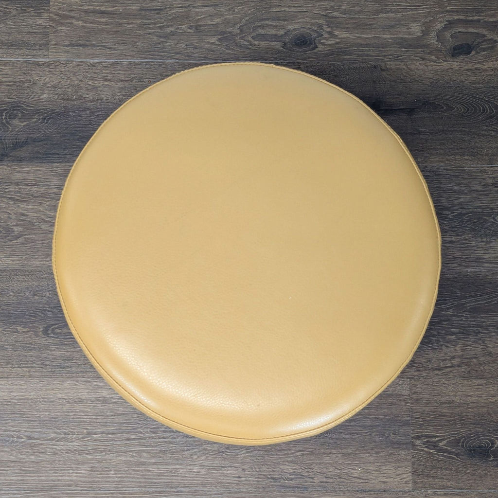 2. Top-down view of a circular tan ottoman, showing smooth leather upholstery and plush cushioning by Reperch.