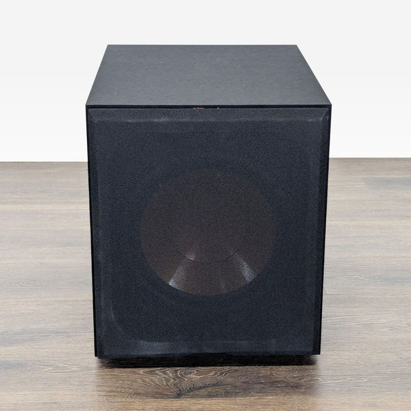 Front view of a black Klipsch subwoofer with a mesh grill, showing a sturdy, box-shaped audio design.