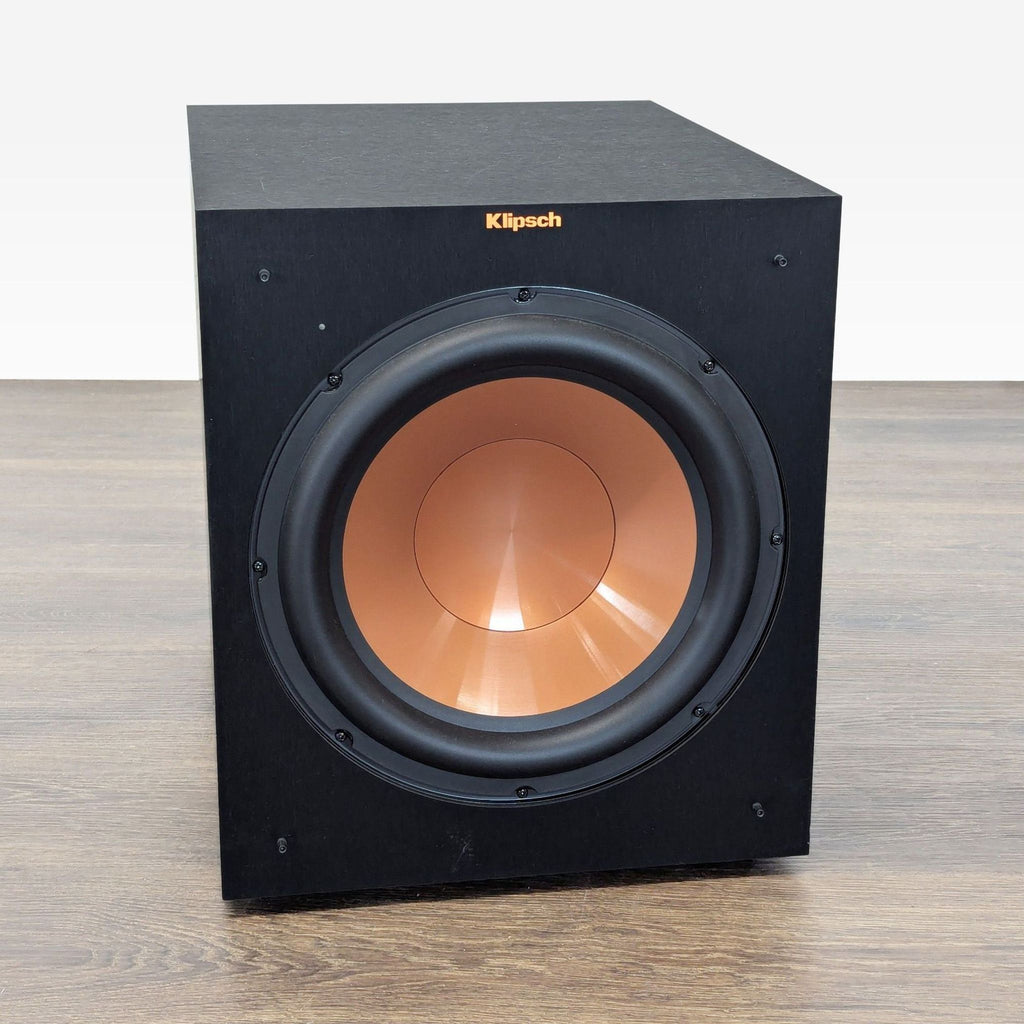 Angled view of a Klipsch subwoofer with a copper-colored driver and visible brand logo, ideal for deep bass sound.