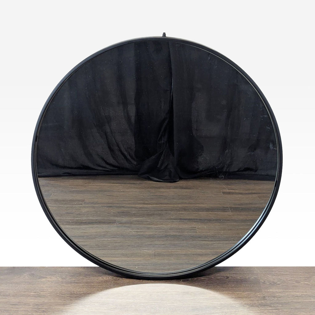 1. Round Reperch mirror with a black metal frame, reflecting wooden floor and dark fabric backdrop.
