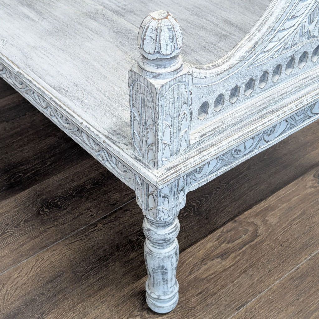 1. Close-up of a Living Spaces bench leg with distressed white wood finish and detailed carved accents.