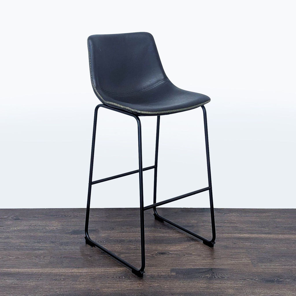 2. Living Spaces bar stool with a sleek black seat and metal frame, angled side view on dark wood flooring.