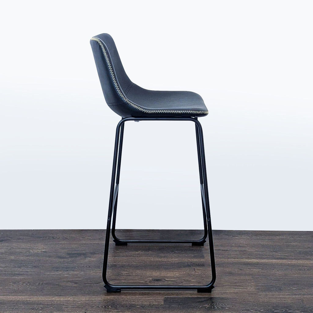 3. Side profile of a Living Spaces black metal frame stool, highlighting its minimalist design and stitching.
