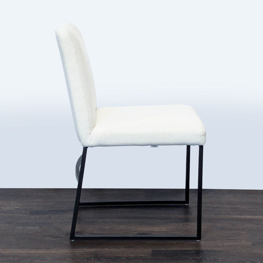 3. Side view of a West Elm dining chair with a minimalist dark bronze frame and white seat and backrest.