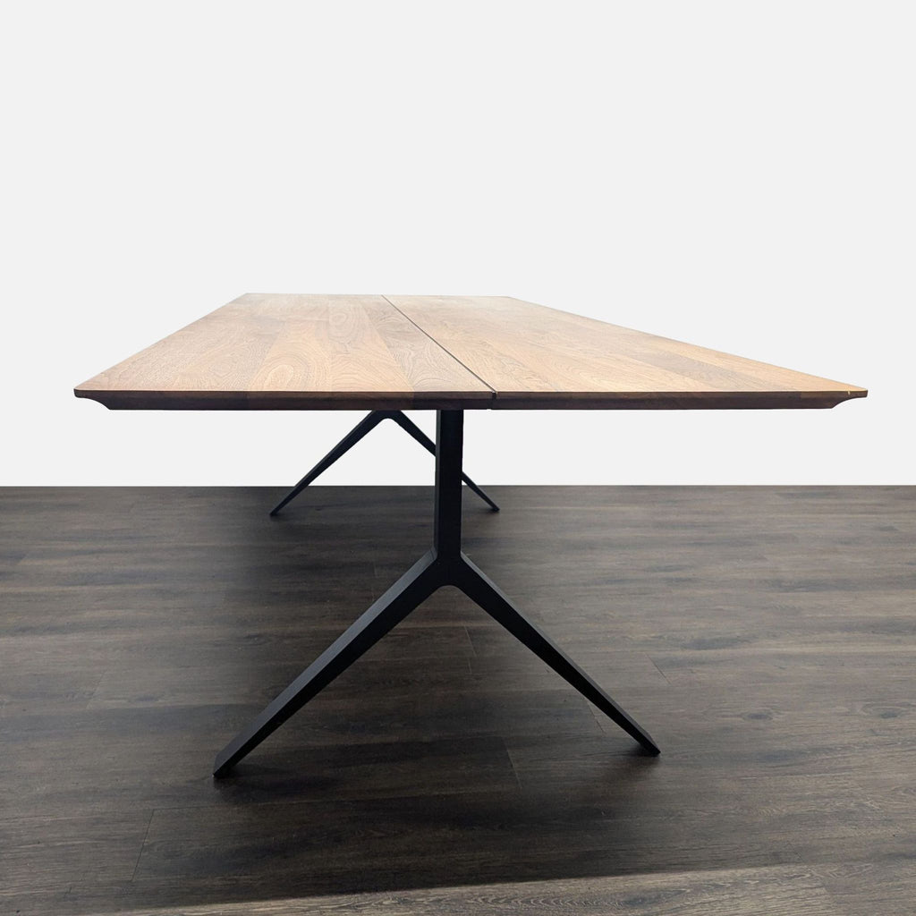 2. Front view of a De La Espada dining table, featuring a sleek wooden surface and angled black metal legs.