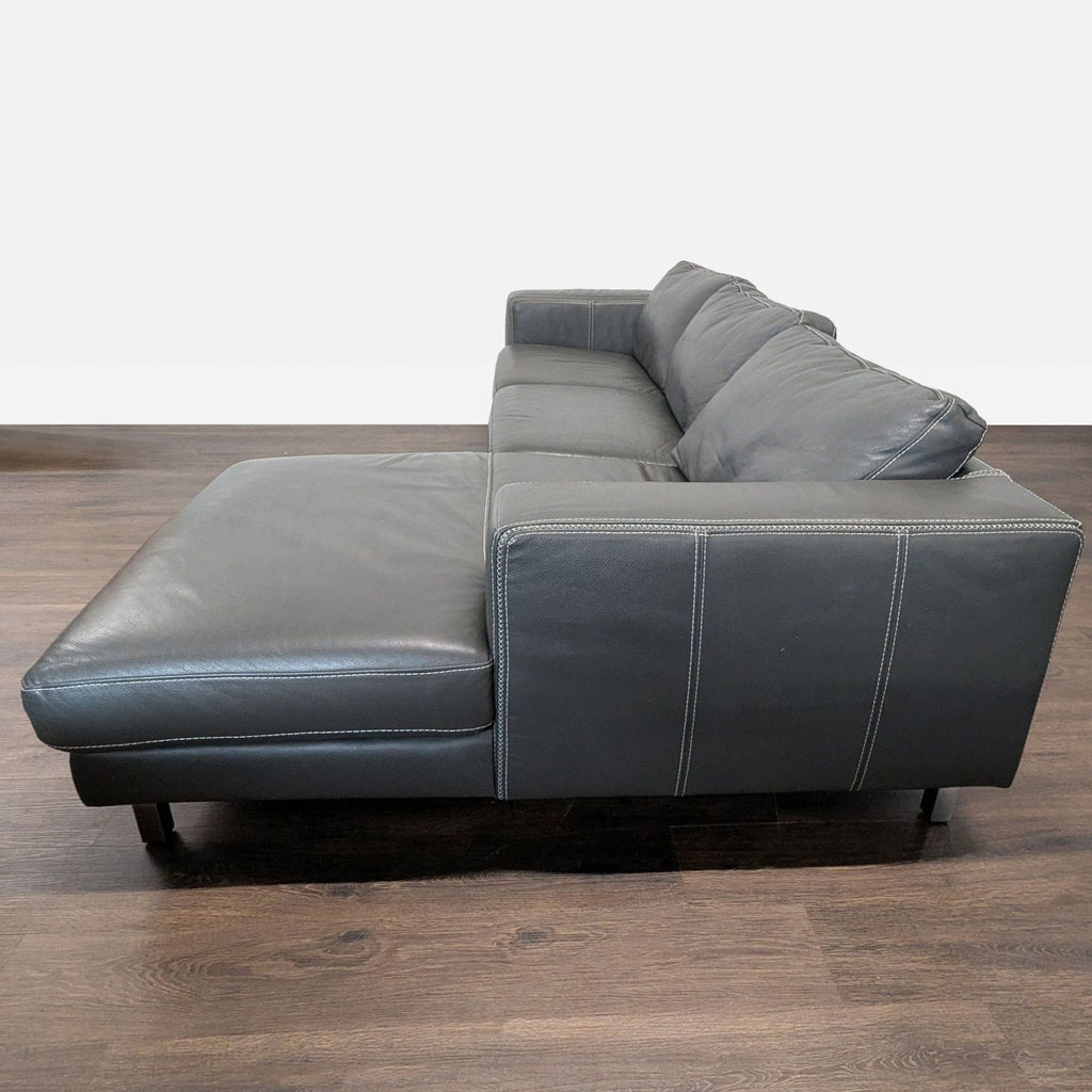1. Side view of a modern Reperch sectional sofa in dark grey leather with chaise, on a wooden floor.