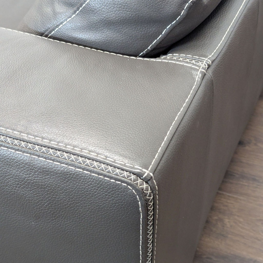 2. Close-up of the Reperch sectional's dark grey leather armrest and cushion details with white stitching.