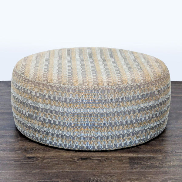 Round ottoman by Room & Board with beige and gray zigzag pattern, pictured on dark wood floor.
