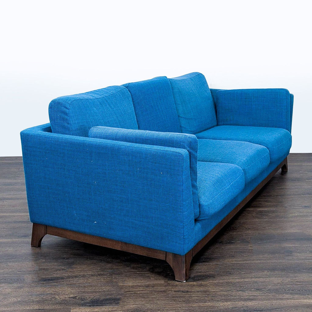 2. Side angle of Article 3-seat blue sofa, showing thick cushions and boxy armrests over dark wood legs.  