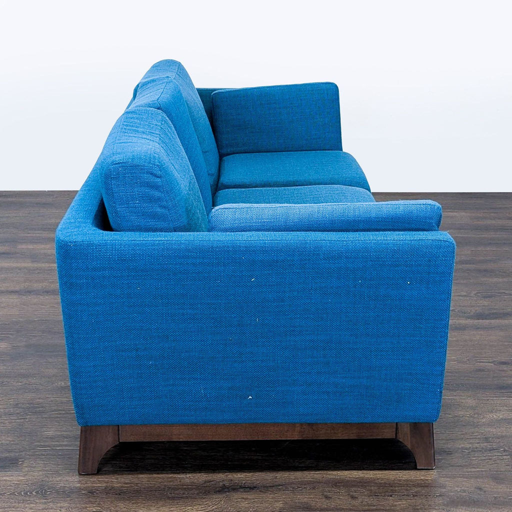 3. Article 3-seat sofa with bright blue upholstery and wooden legs, shown from the side for profile detail.