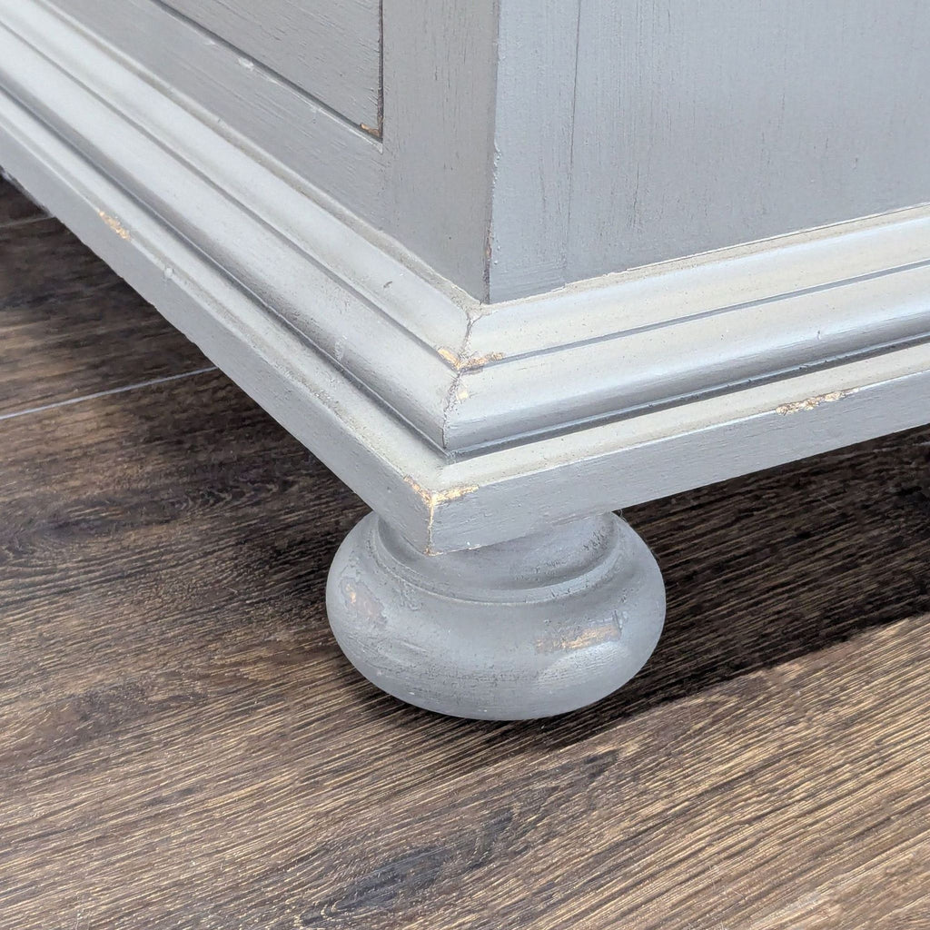 3. Close-up of the corner and bun foot of a gray Restoration Hardware dresser, showing distressed finish and wood grain.