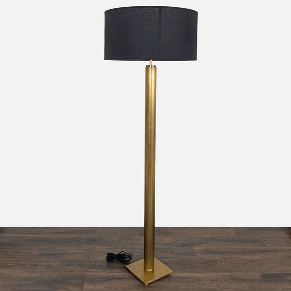 Modern floor lamp with brass base and black drum shade, ideal for stylish living rooms or offices.